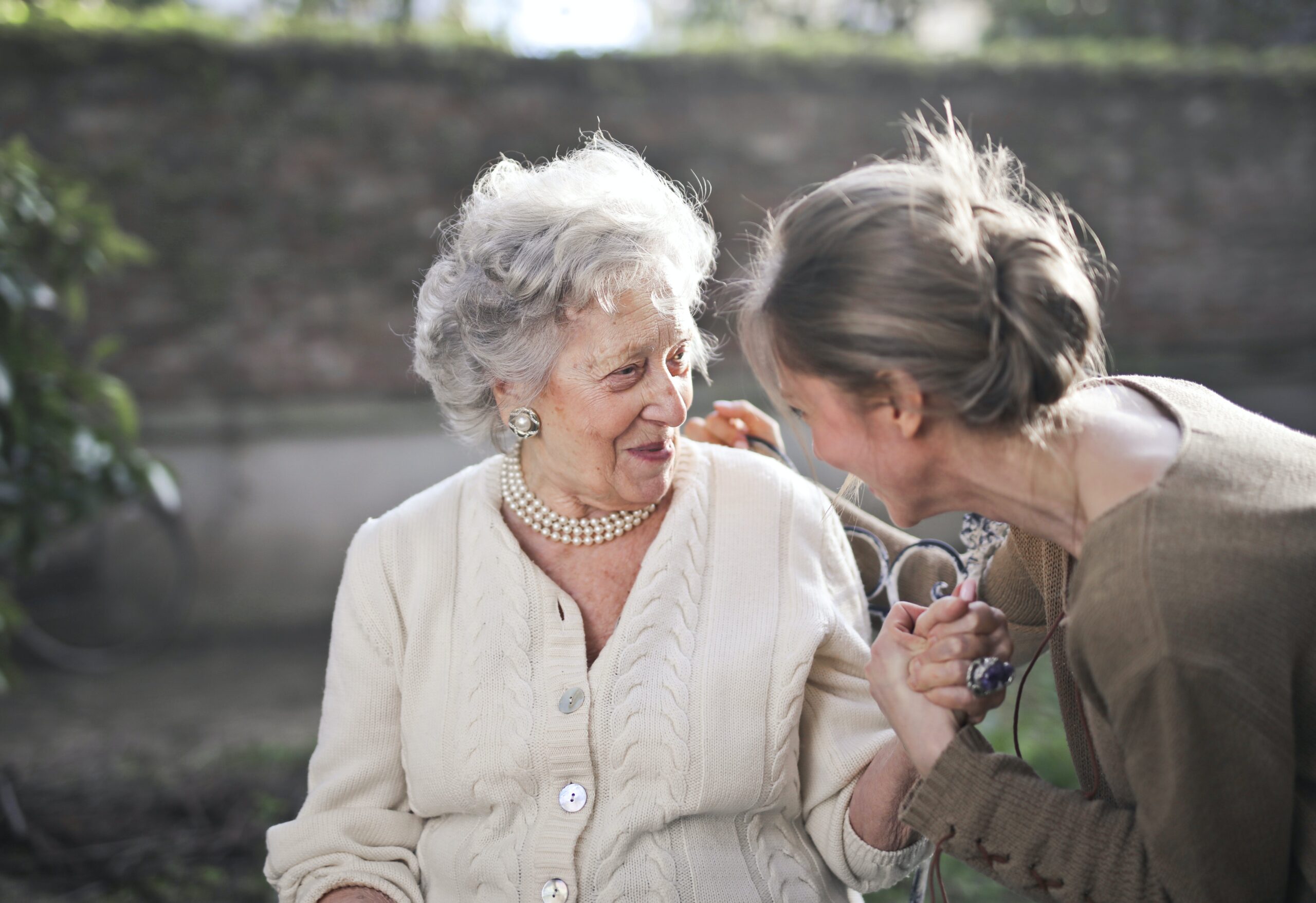 An older woman smiles as her daughter holds her hand.