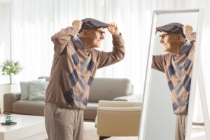 An older gentleman wearing the best adaptive clothing for seniors smiles at his reflection in the mirror.