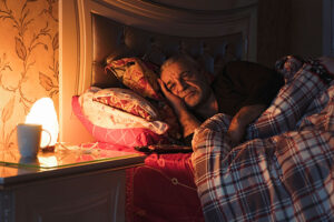 A man with insomnia lies in bed, trying to think of ways to improve sleep for older adults.