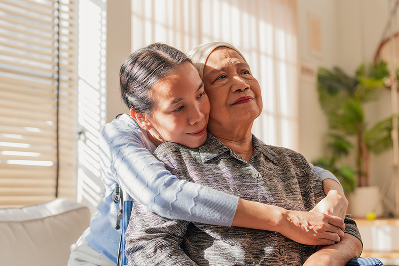 A woman hugs her aging mother and thinks about the importance of emotional support for cancer caregivers.