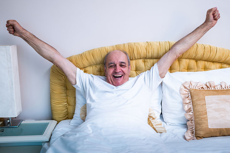 A man stretches while waking up well rested because he found senior sleep solutions that work for him.
