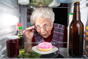 A woman eyes a sugary donut in her fridge, highlighting the importance of preventing food addiction in seniors.