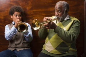 An older man practices playing the trumpet with his grandson, as it is one of the best cognitive exercises for aging parents.