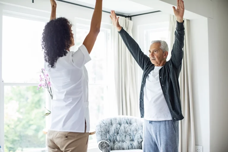 A caregiver shows a gentle exercise for seniors to increase strength and mobility to her elderly client.