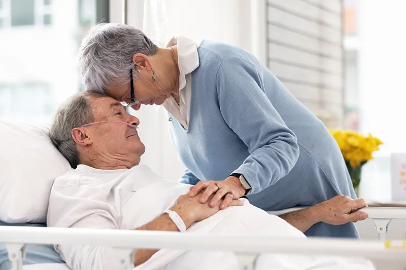 A wife offers reassurance to her husband as he receives dementia hospital care.