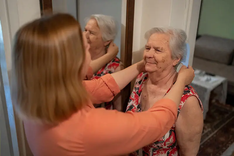 An adult daughter notices senior skin changes while helping her mother get ready at home.
