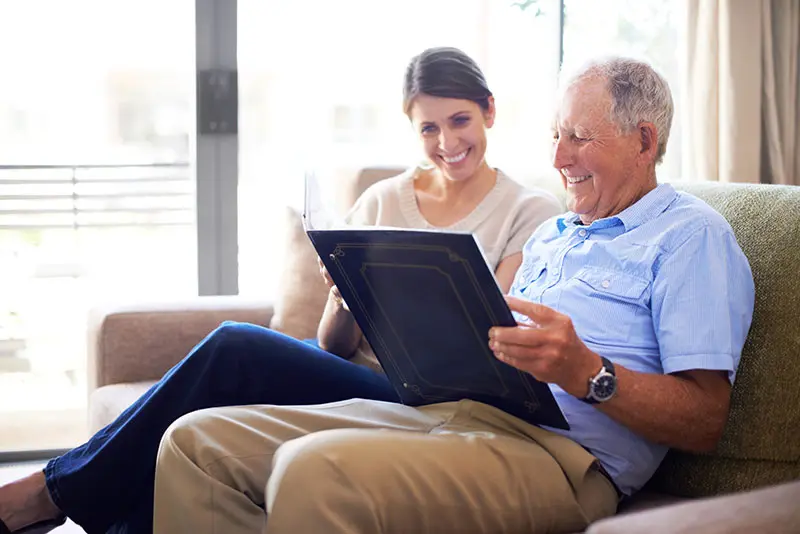An older adult looks through a photo album with his daughter, demonstrating the benefits of reminiscing for seniors.